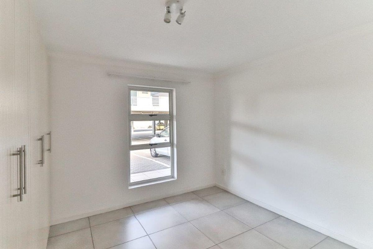 A bright, empty bedroom featuring neutral floor tiles and built-in cupboards, offering a clean and versatile space.