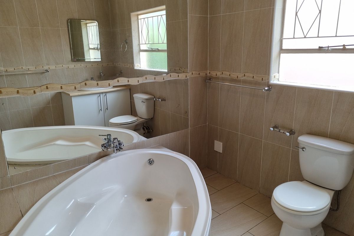 A functional bathroom featuring a built-in bathtub, a vanity cabinet with a basin, and a toilet, finished with neutral wall and floor tiling.