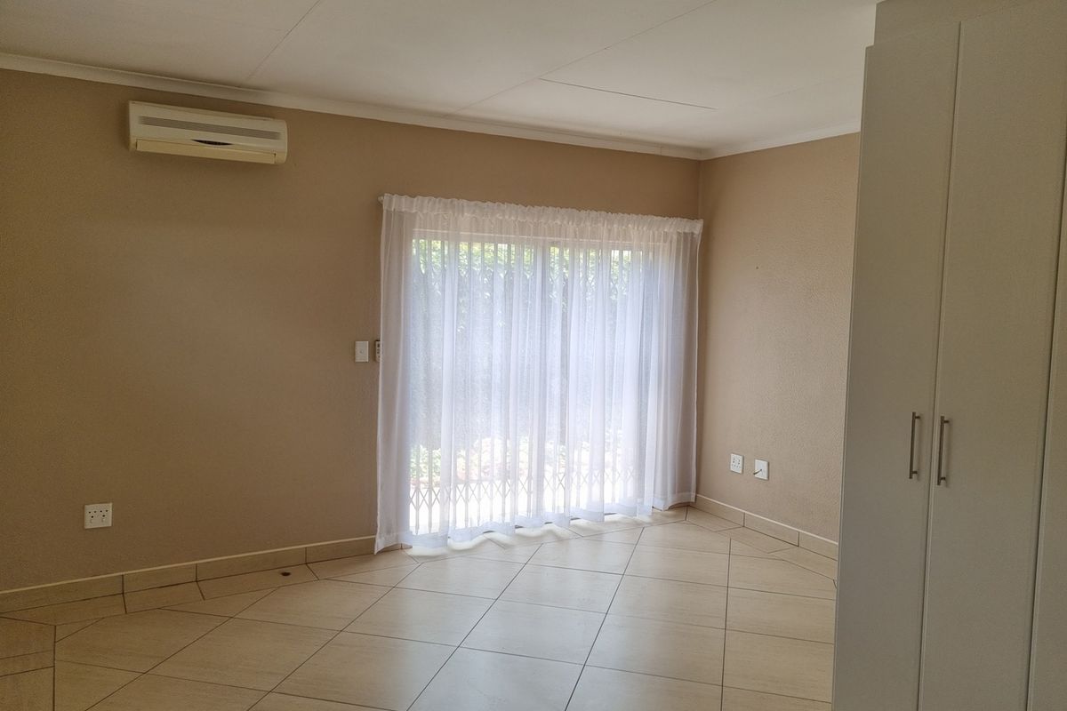 A bright, empty bedroom featuring tiled flooring, built-in cupboards, and a wall-mounted air conditioning unit with sliding door access to the exterior.