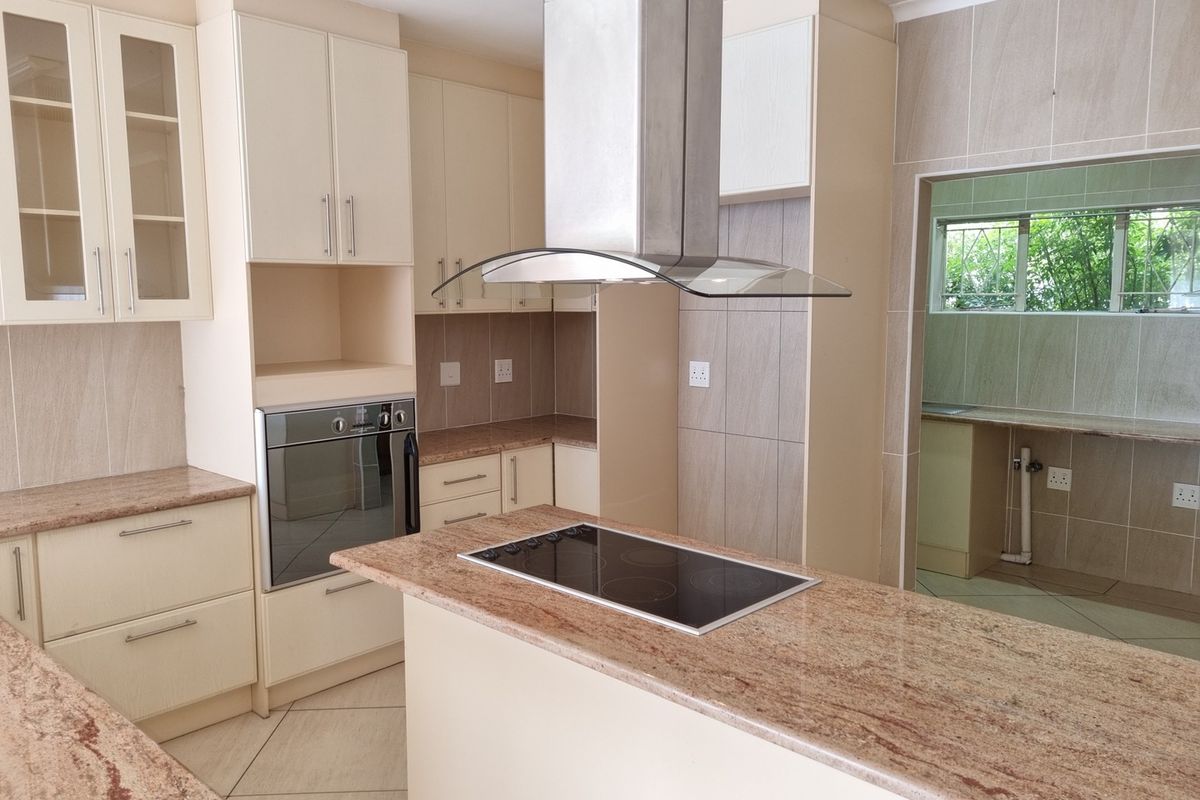 Modern kitchen featuring granite countertops, a central island with a built-in electric hob, stainless steel extractor fan, and integrated oven.