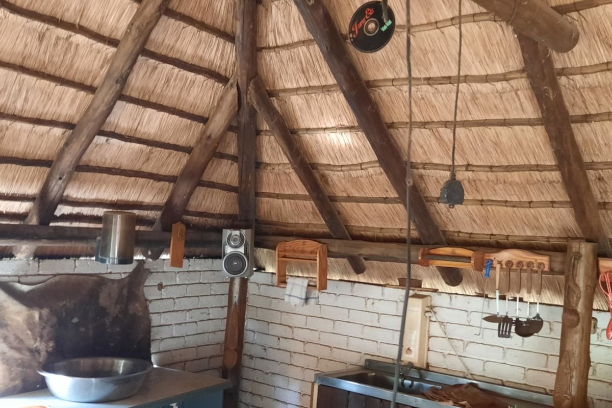 Rustic outdoor kitchen area featuring a traditional thatched roof, exposed brick walls, and a built-in sink unit with wooden cabinetry.