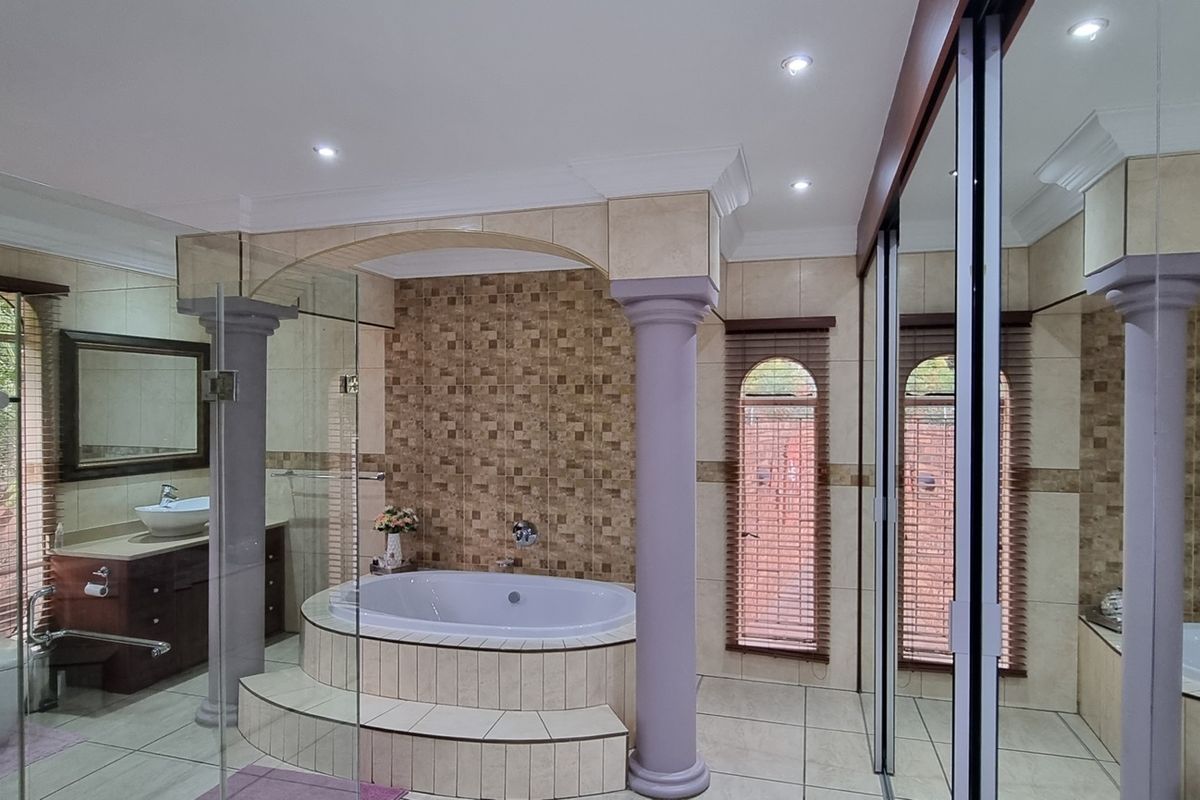 Spacious bathroom featuring a raised built-in bathtub, decorative columns, vanity with vessel sink, and large mirrored wardrobe doors.