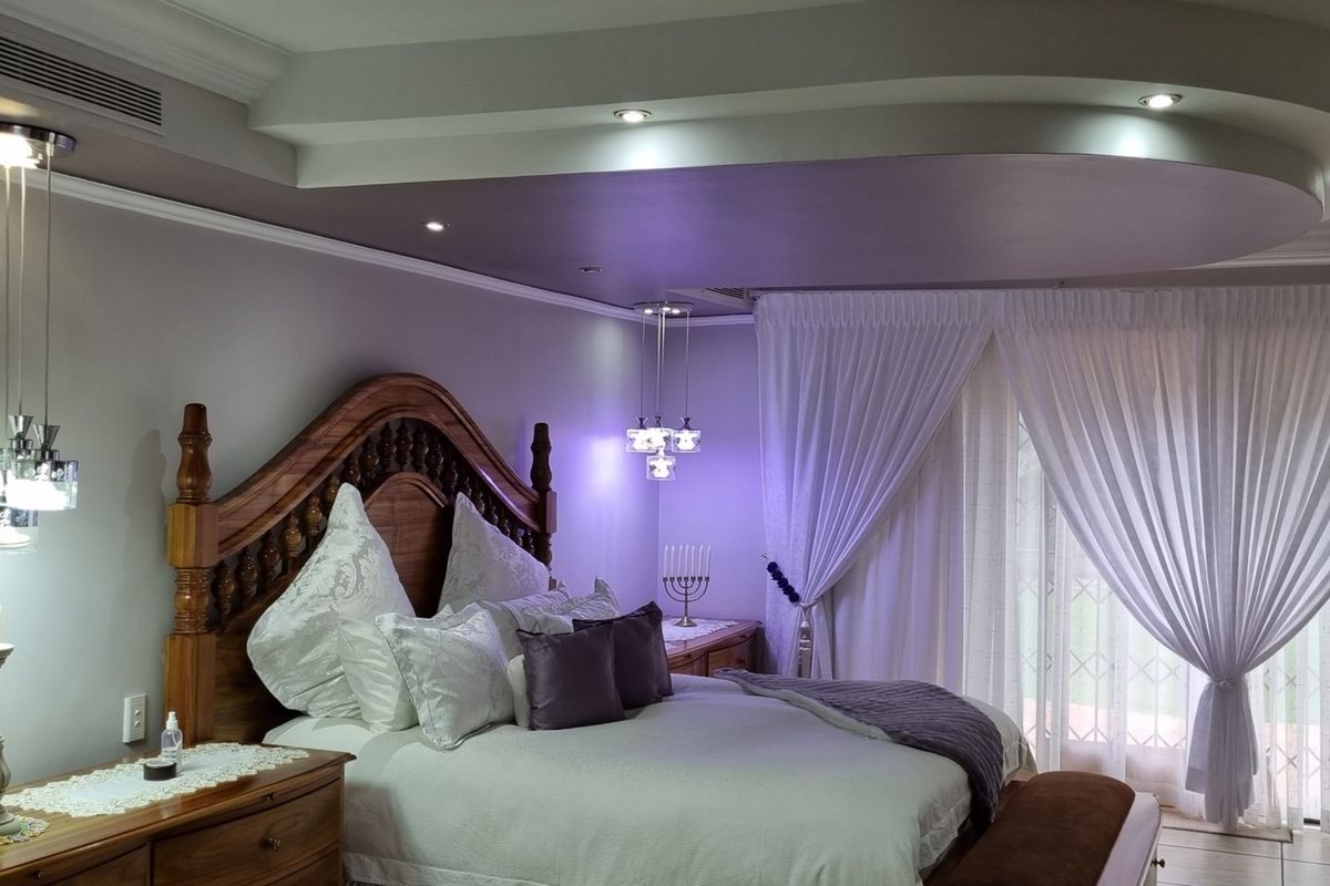 Spacious bedroom featuring a decorative recessed ceiling with integrated downlights, pendant lighting, and large sliding glass doors leading to the exterior.