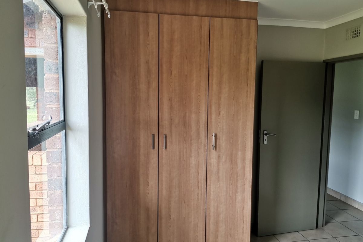 A bedroom featuring built-in wooden cabinetry, tiled flooring, and a window with a view of the exterior brickwork.