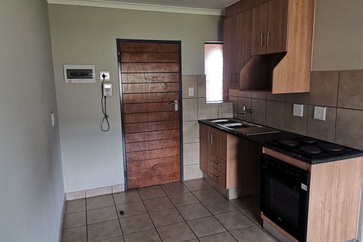 Compact kitchen featuring wood-finish cabinetry, integrated oven and hob, tiled splashbacks, and tiled flooring, with direct access to an exterior door.