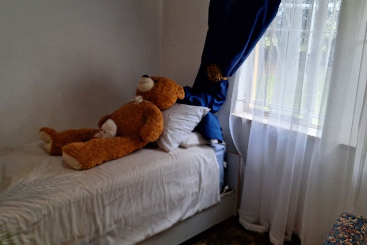 A bedroom featuring a window with security bars and curtains.
