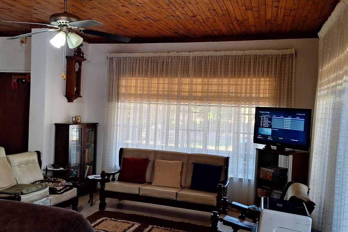 A living room featuring a warm timber tongue and groove ceiling, a ceiling fan, and large windows dressed with sheer curtains.