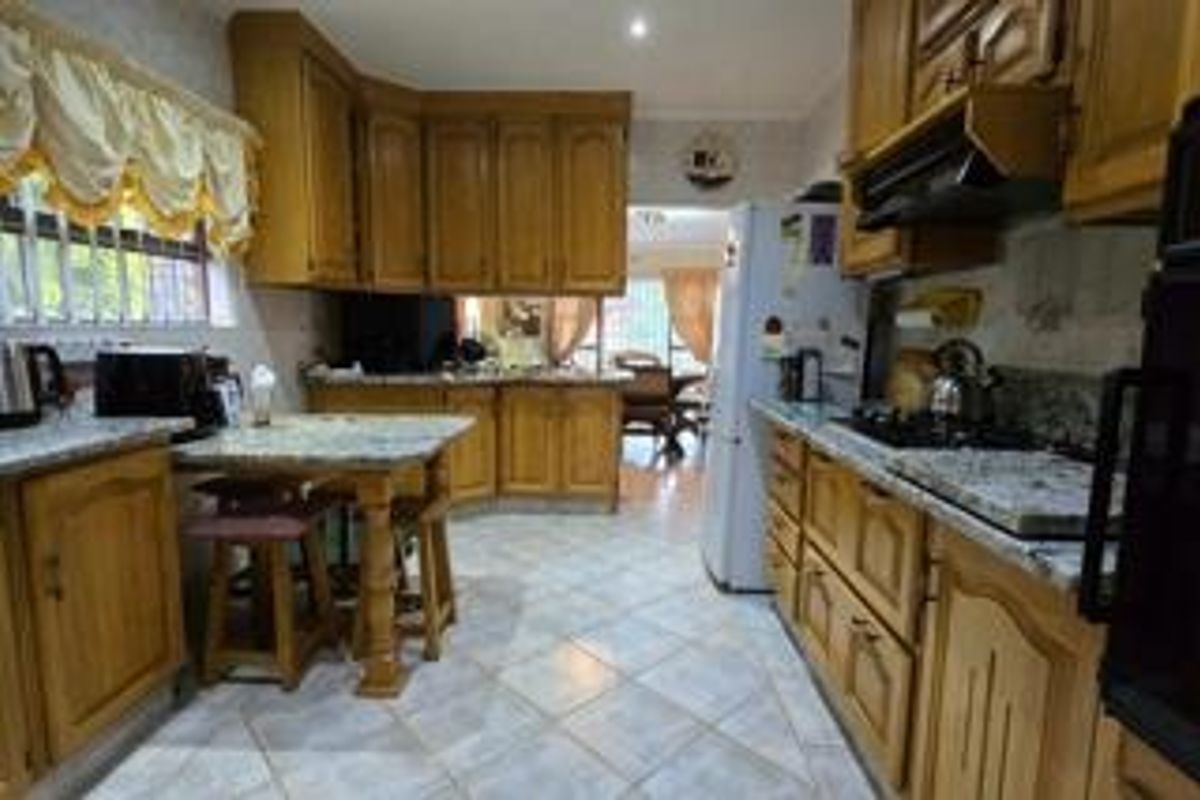A traditional kitchen featuring wooden cabinetry, granite countertops, a built-in hob, and tiled flooring, offering a functional layout with potential for modernization.