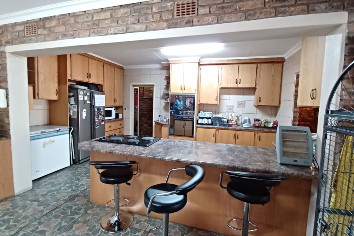 A functional kitchen featuring wooden cabinetry, a breakfast bar with a stone-look countertop, built-in oven, and exposed brick wall detailing.