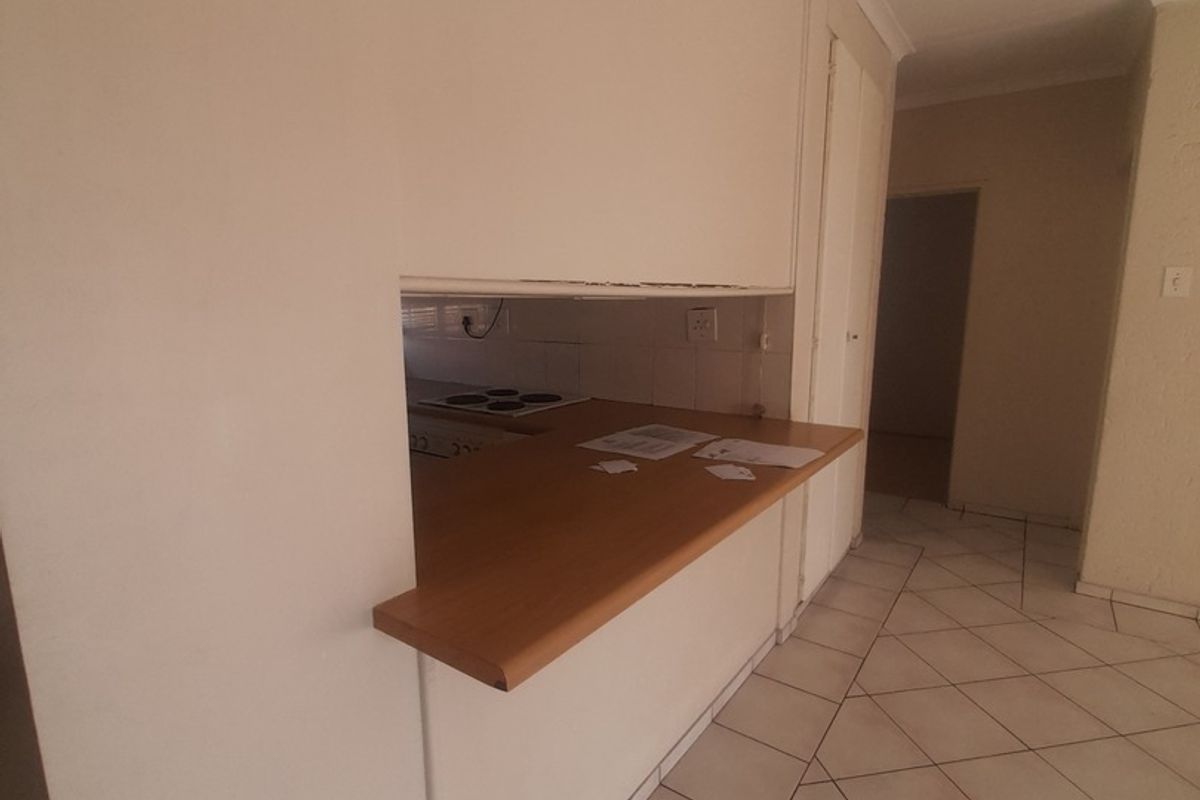 A view of the kitchen pass-through window with a wooden breakfast bar, featuring tiled flooring and a neutral interior layout.