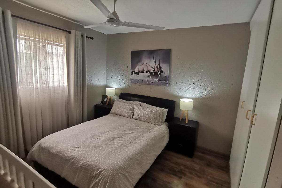 A cozy bedroom featuring wood-look flooring, a ceiling fan, and built-in wardrobe storage with neutral wall tones.