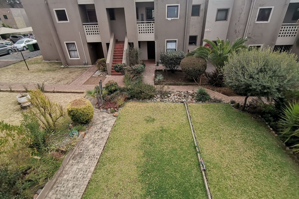 An elevated view of the apartment complex rear exterior, featuring a shared garden area, paved walkways, and multi-level residential units.