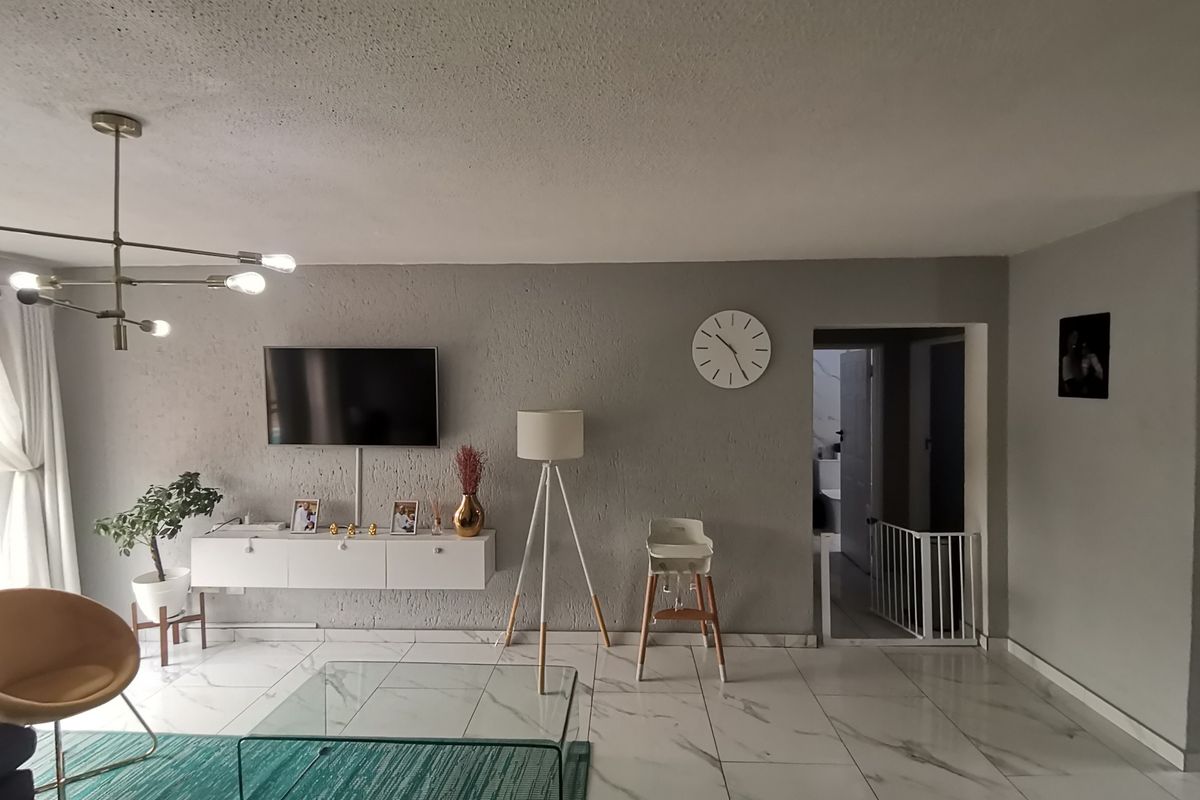 A modern living room featuring large format marble-look floor tiles, a contemporary chandelier, and a wall-mounted media console.