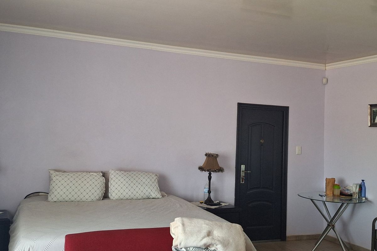 A spacious bedroom featuring neutral wall tones, crown molding, and a functional layout with direct access to an internal door.