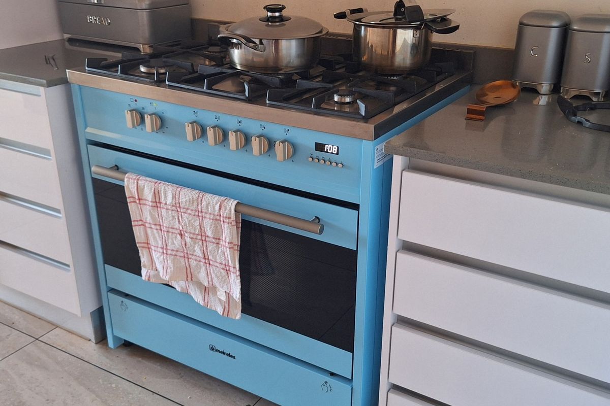 A modern kitchen featuring a distinctive blue freestanding gas stove and oven, complemented by stone countertops and clean white cabinetry.