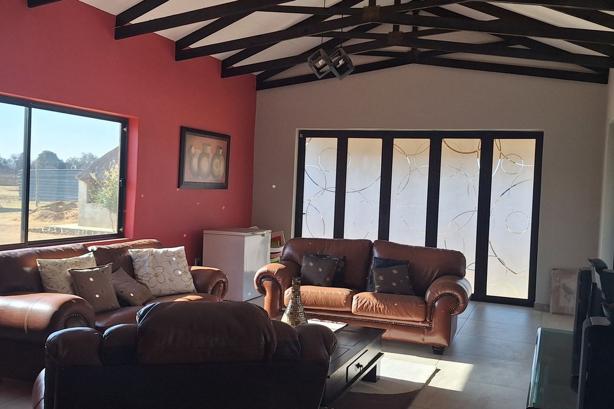 Spacious living room featuring high vaulted ceilings with exposed timber trusses, tiled flooring, and large windows providing ample natural light.