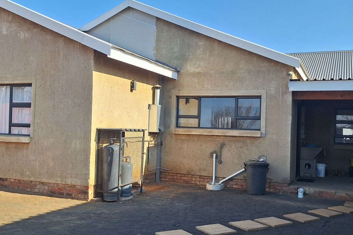 Rear exterior view of the property featuring a corrugated metal roof, aluminium window frames, and a covered patio area with exposed brickwork.