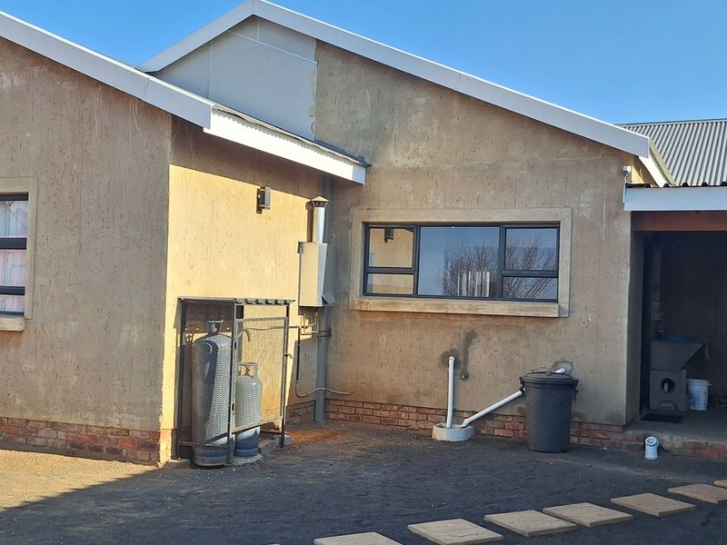 Rear exterior view of the property featuring a corrugated metal roof, aluminium window frames, and a covered patio area with exposed brickwork.