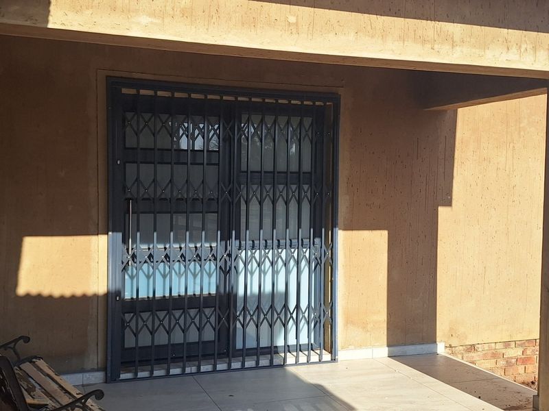 A covered patio area featuring tiled flooring, concrete pillars, and a secure metal gate entrance to the main dwelling.