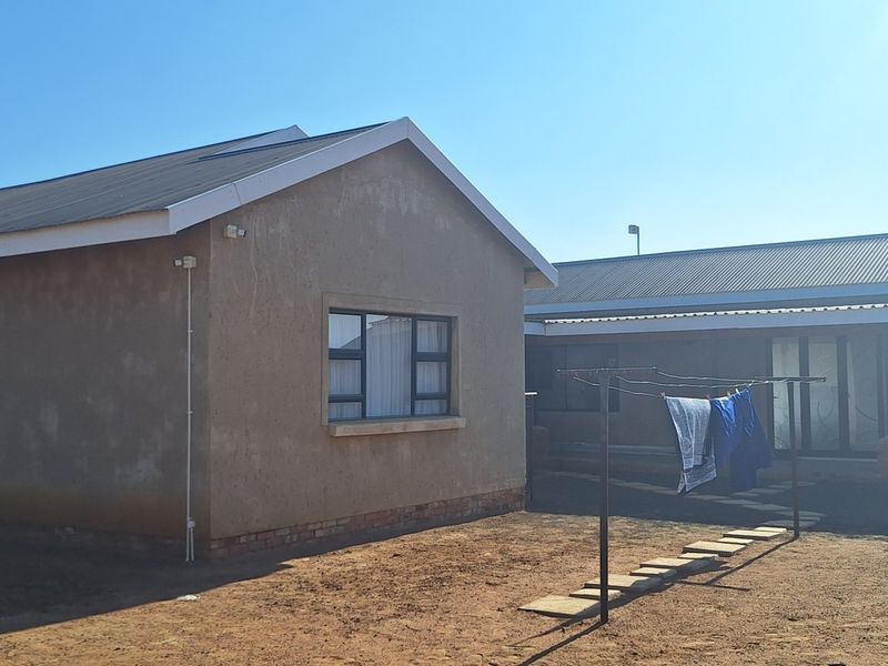 Rear view of the property showing plastered exterior walls, corrugated metal roofing, and a covered patio area.