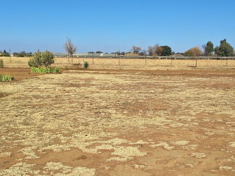Expansive open land area on a small holding, featuring dry grass, perimeter fencing, and distant agricultural structures.