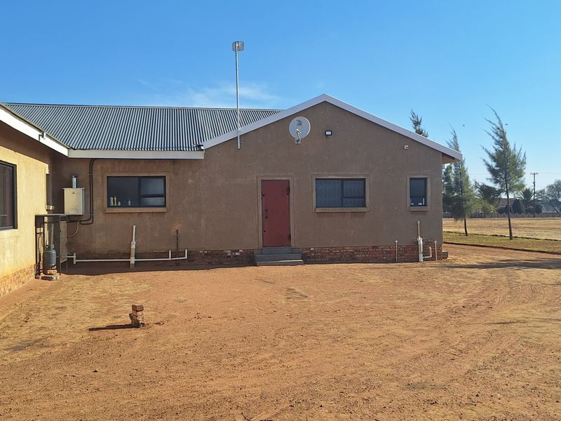 Rear view of the property featuring plastered walls, a corrugated metal roof, and an open yard area with exposed utility connections.