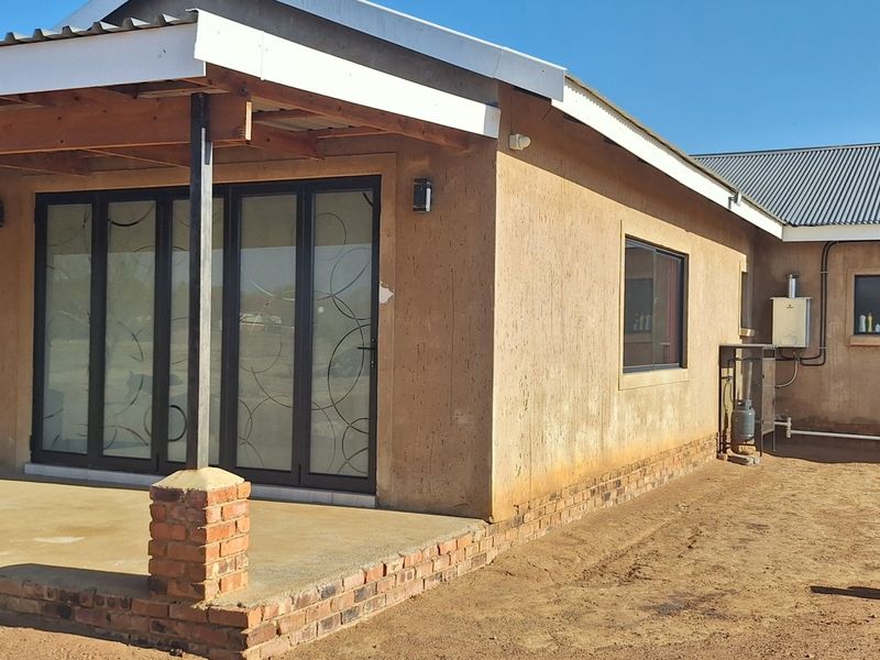 Rear view of the property featuring a covered patio with brick pillars, aluminium stacker doors, and an external gas geyser installation.