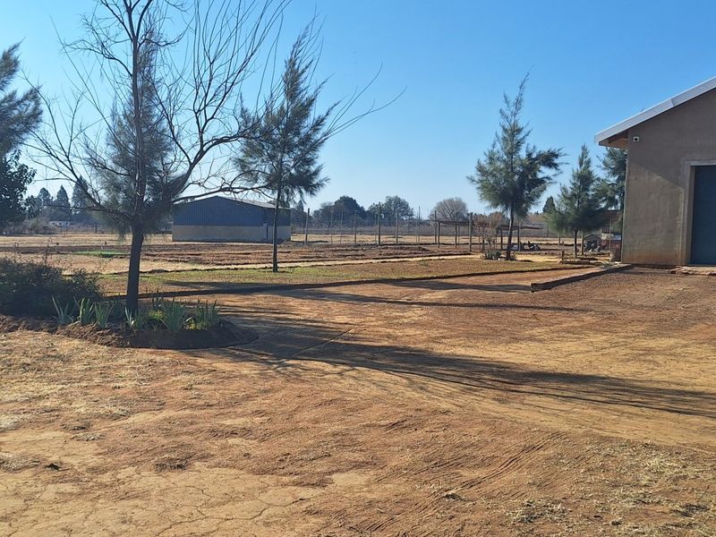 Spacious small holding grounds featuring a large garage structure, open land, and an additional outbuilding in the distance.