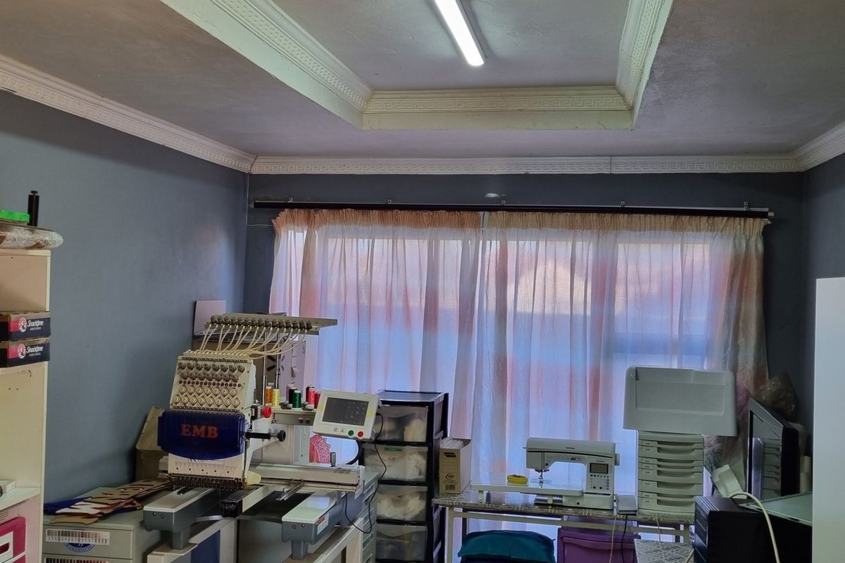 A functional room currently utilized as a workspace, featuring decorative ceiling cornices and a large window with curtain track.