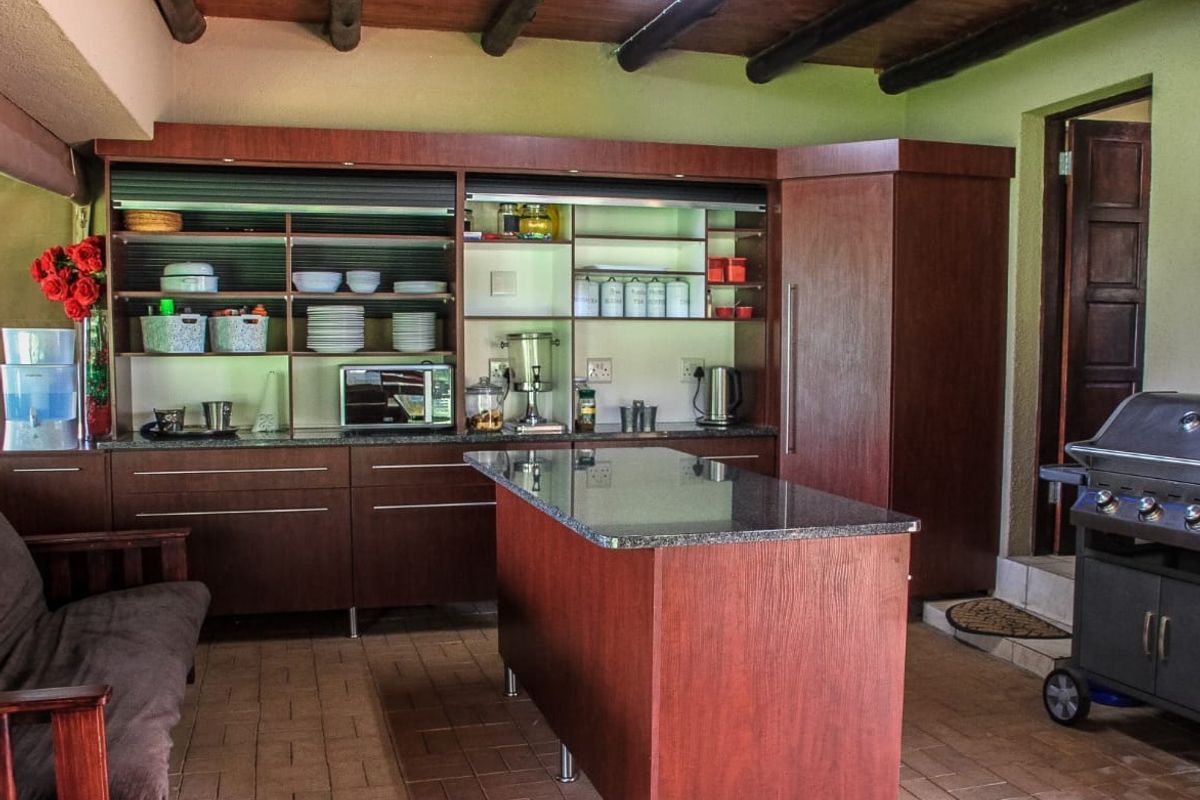 A functional kitchen featuring dark wood cabinetry, granite countertops, a central island, and rustic exposed timber ceiling beams.