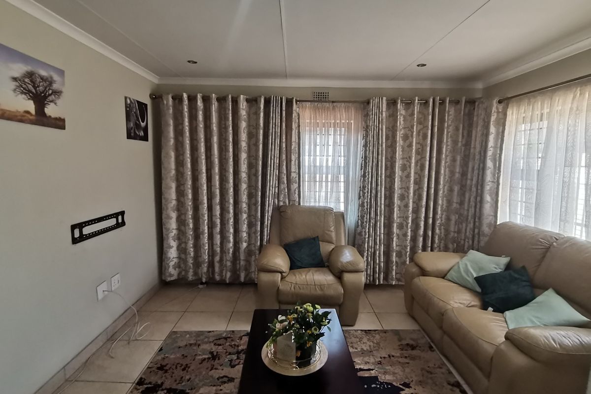 A comfortable living room featuring tiled flooring, recessed ceiling lighting, and large windows dressed with floor-to-ceiling curtains.