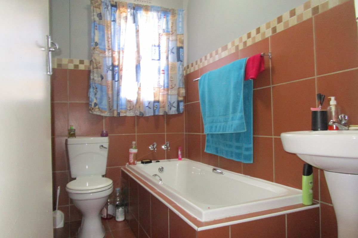 A functional bathroom featuring a built-in bathtub, pedestal basin, and toilet, finished with terracotta-colored wall tiles and a decorative border.