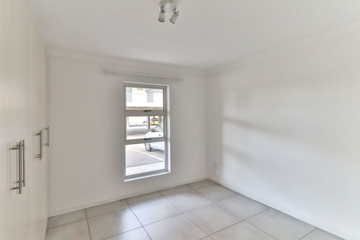 A bright, empty bedroom featuring neutral floor tiles and built-in cupboards, offering a clean and versatile space.