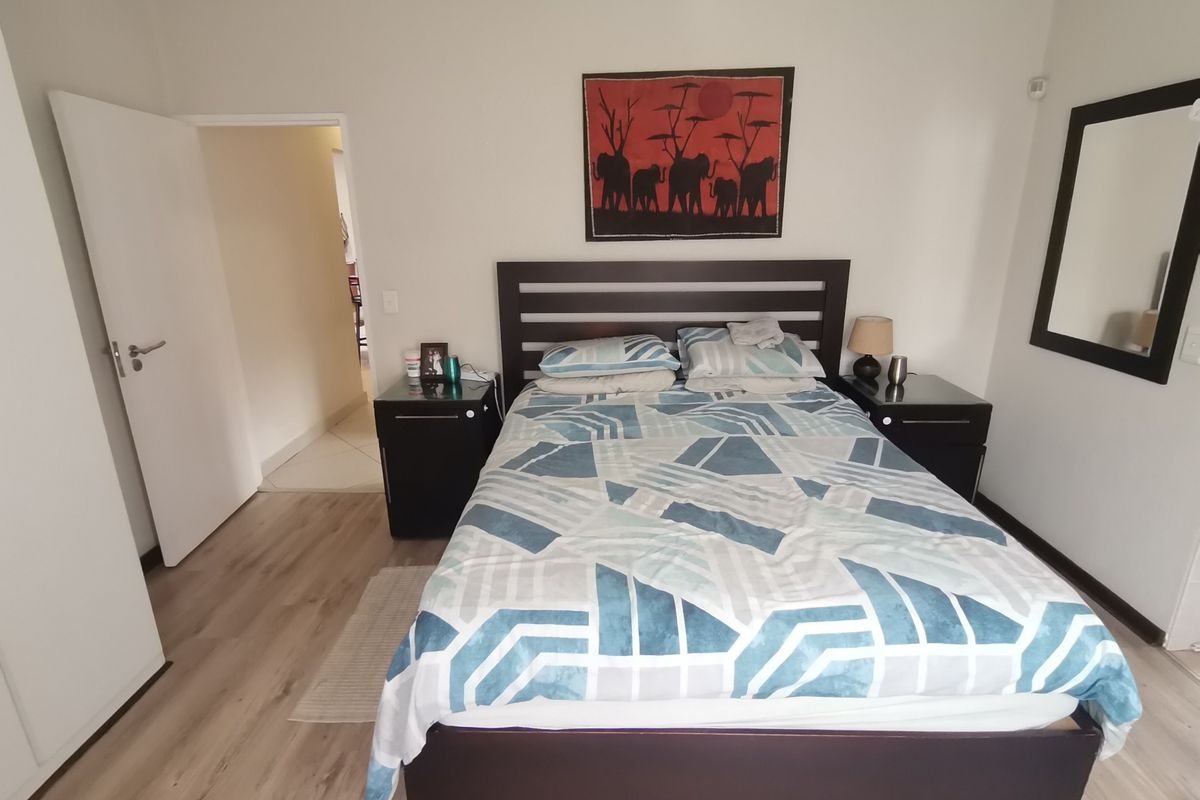 A well-maintained bedroom featuring light wood-look laminate flooring, neutral walls, and a doorway leading to an adjacent hallway.