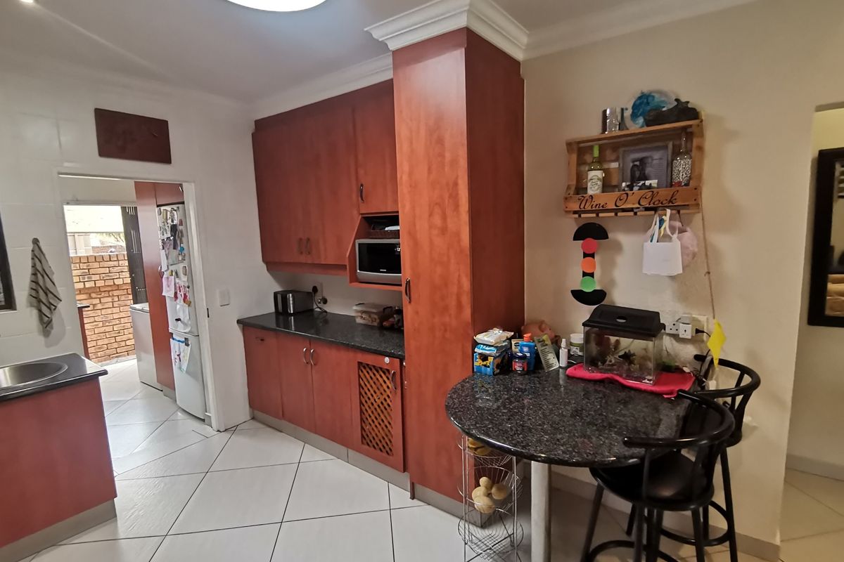 A functional kitchen featuring cherry-wood cabinetry, granite countertops, and tiled flooring, with an adjacent scullery area visible through the doorway.