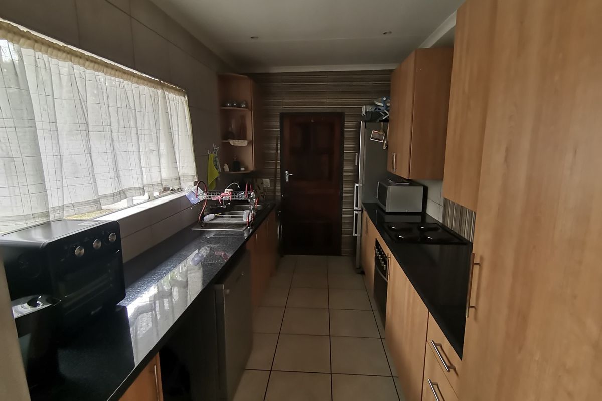 A functional galley-style kitchen featuring dark granite countertops, light wood-toned cabinetry, tiled flooring, and a built-in hob and oven.
