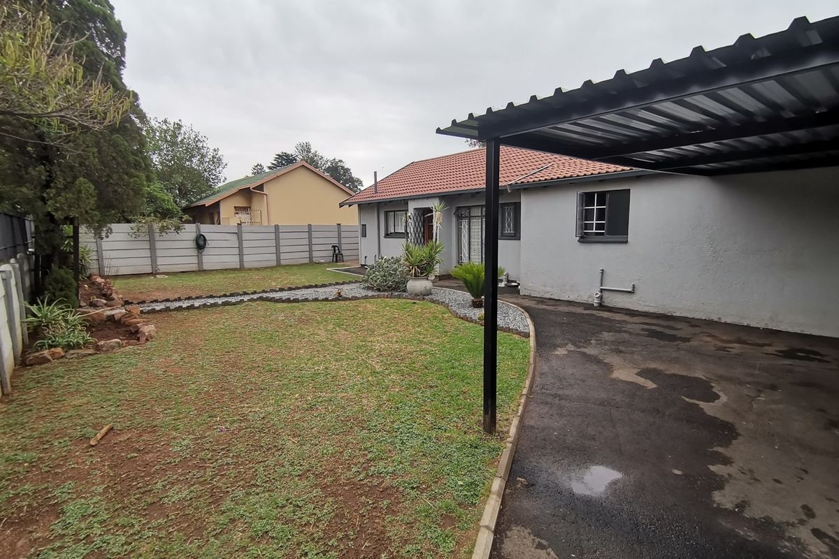A view of the rear garden featuring a paved driveway, a covered carport structure, and a perimeter wall.