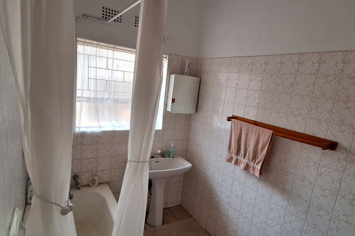 A functional bathroom featuring a pedestal basin, bathtub with shower curtain, and wall-mounted medicine cabinet, finished with dated ceramic wall tiles.