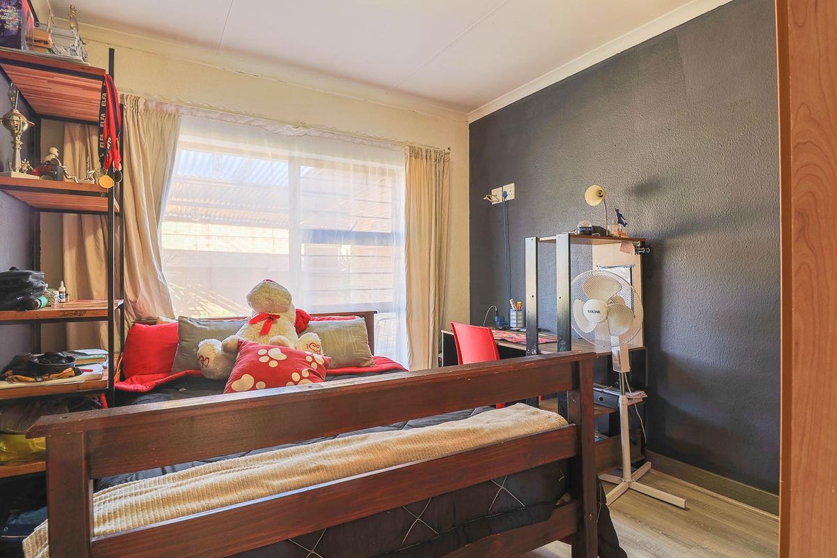 A bedroom featuring a dark accent wall, laminate flooring, and a large window allowing natural light.