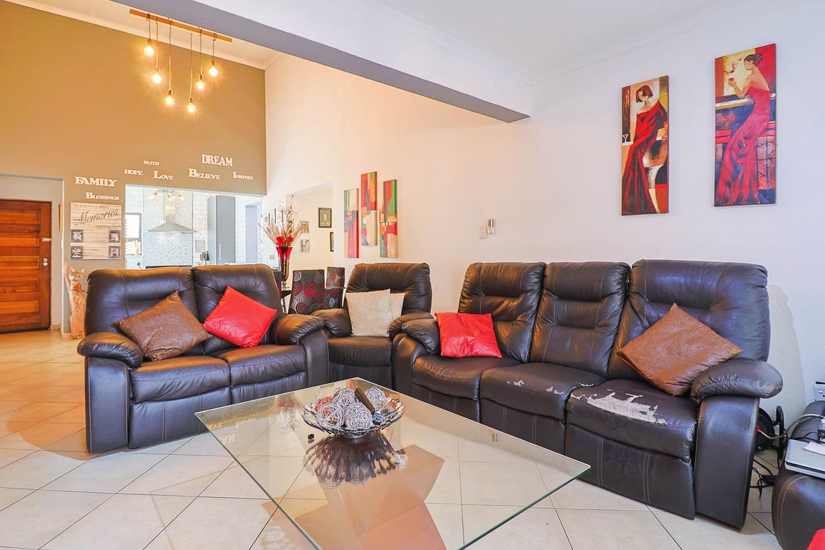 Spacious living area featuring tiled flooring, high ceilings with pendant lighting, and an open-plan layout connecting to the kitchen area.
