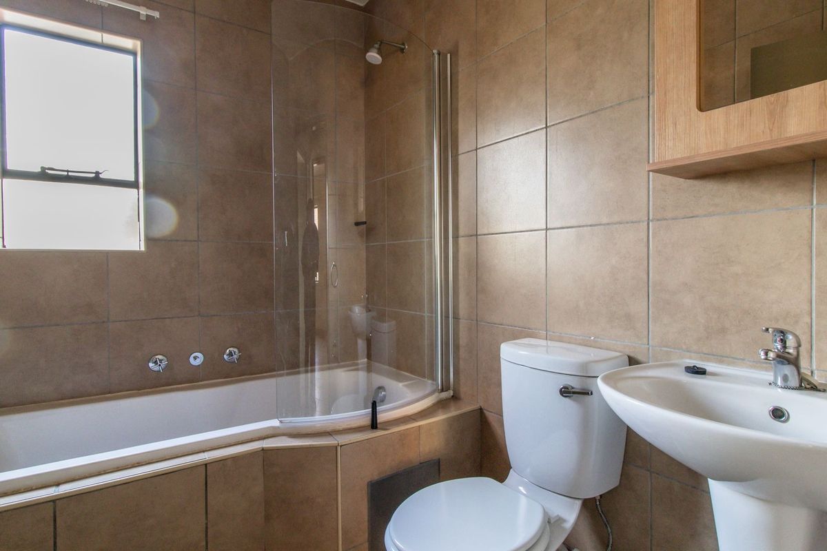 A functional bathroom featuring a combined shower and bathtub, a pedestal basin, and a toilet, finished with neutral wall tiles.