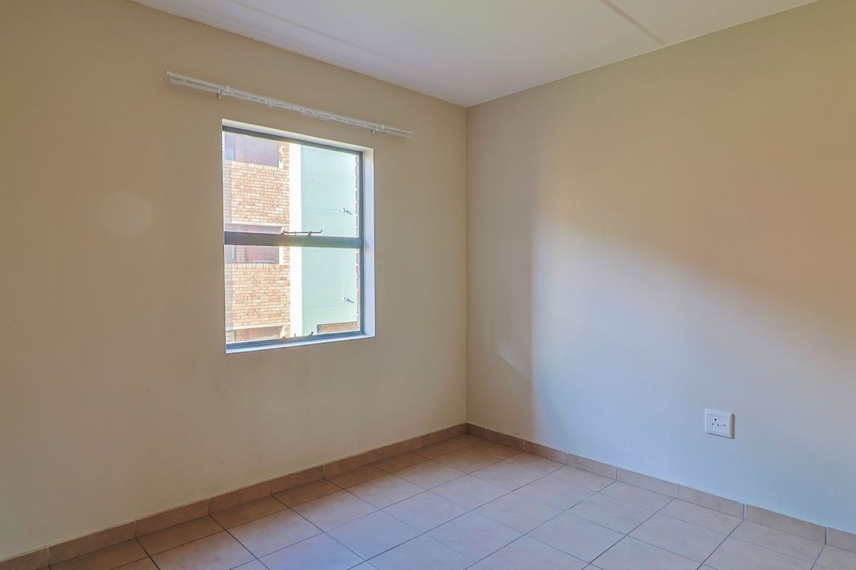 A bright, empty bedroom featuring neutral wall paint, tiled flooring, and a window with a curtain rail.