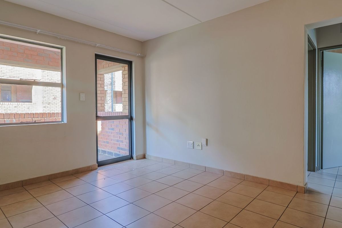 An empty living room featuring neutral tiled flooring, a glass door leading to an outdoor area, and access to an adjacent hallway.