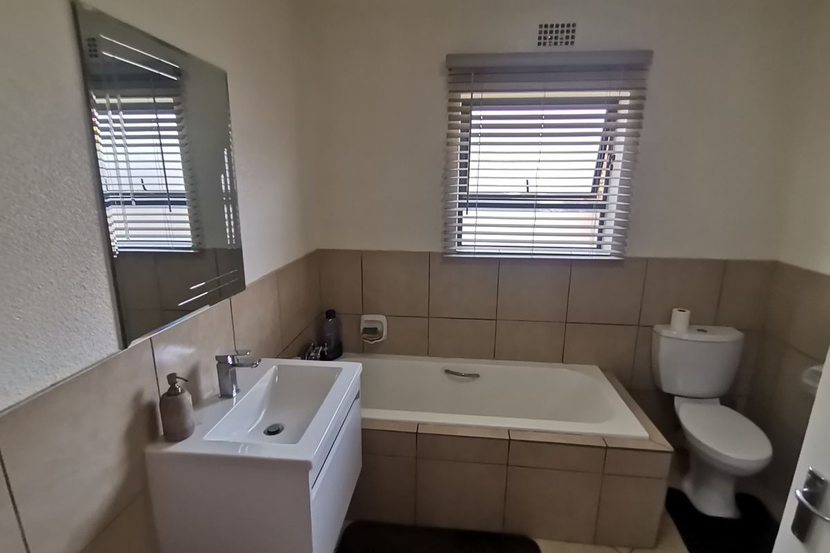A functional bathroom featuring a built-in bathtub, a modern vanity basin, a toilet, and neutral wall tiling with a window for natural light.