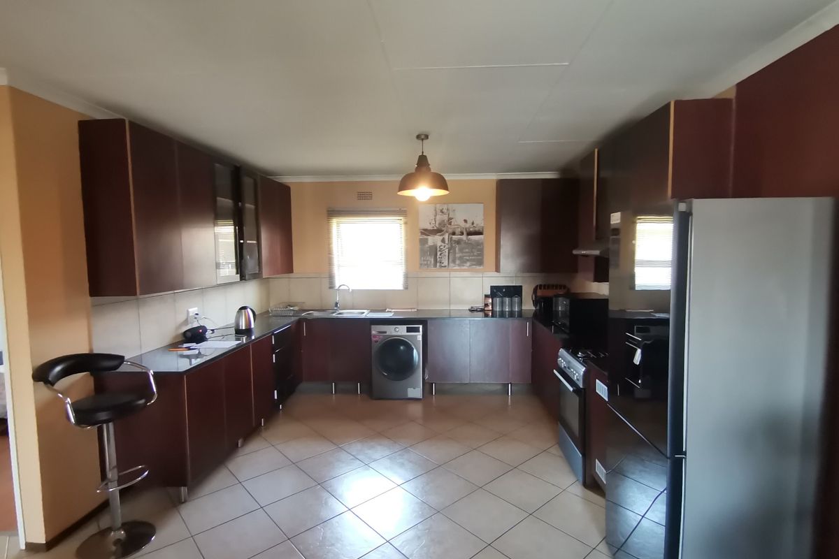 A functional kitchen featuring dark wood cabinetry, tiled flooring, integrated oven and hob, and a dedicated space for a washing machine.
