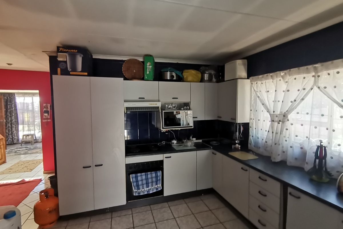 A functional kitchen featuring white cabinetry, dark countertops, a built-in oven, and tiled flooring, with an adjacent view into the living area.