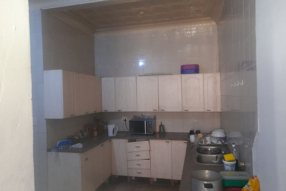A functional kitchen featuring light-toned cabinetry, a double-basin sink, and tiled walls, requiring some maintenance and cosmetic updates.