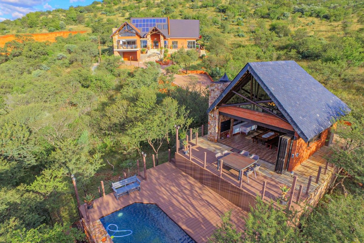 Aerial view of a property featuring a main house with solar panels and a separate entertainment structure with a deck and swimming pool.