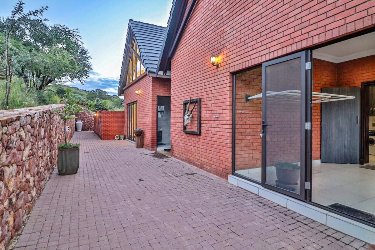 A well-maintained exterior rear view featuring red brick masonry, paved courtyard, and large glass sliding doors leading into the home.