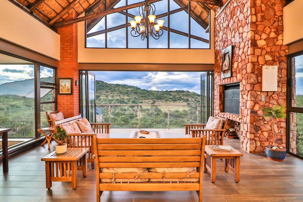 Spacious living area featuring a vaulted timber ceiling, exposed brickwork, a stone fireplace, and large folding doors opening to a scenic balcony.